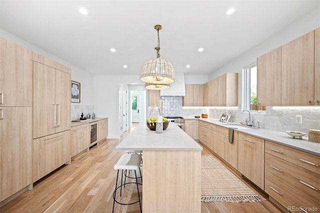 kitchen featuring a center island, backsplash, hanging light fixtures, light brown cabinetry, and light hardwood / wood-style floors