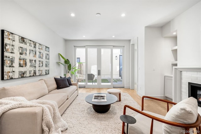 living room with baseboards, french doors, light wood-type flooring, a brick fireplace, and recessed lighting