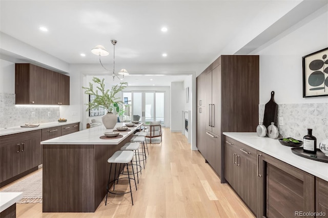 kitchen with dark brown cabinetry, a center island, light countertops, light wood-type flooring, and a kitchen bar