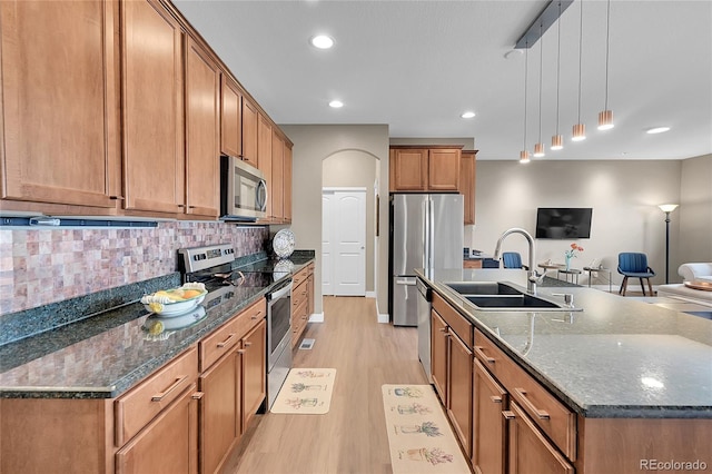 kitchen with appliances with stainless steel finishes, light wood-type flooring, tasteful backsplash, sink, and hanging light fixtures