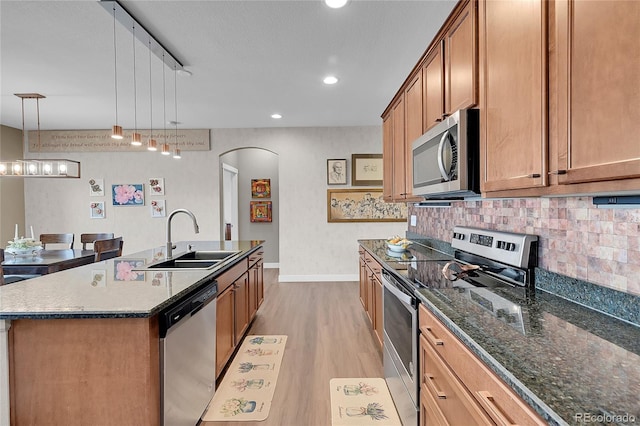 kitchen with sink, hanging light fixtures, light wood-type flooring, an island with sink, and stainless steel appliances