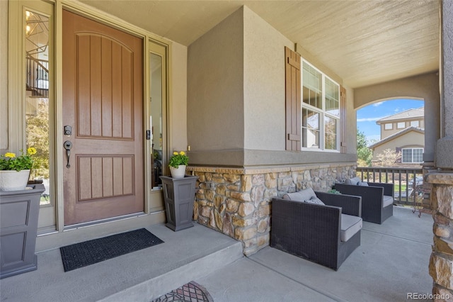 view of exterior entry featuring stone siding, stucco siding, and covered porch