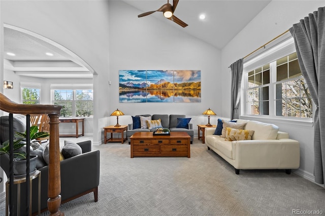 carpeted living area with ceiling fan, baseboards, arched walkways, and high vaulted ceiling