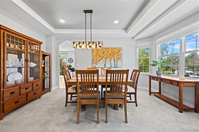 dining area with arched walkways, light carpet, a healthy amount of sunlight, and a tray ceiling