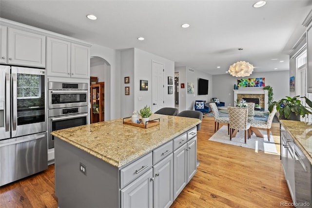 kitchen featuring a center island, light wood-style flooring, a fireplace, arched walkways, and appliances with stainless steel finishes