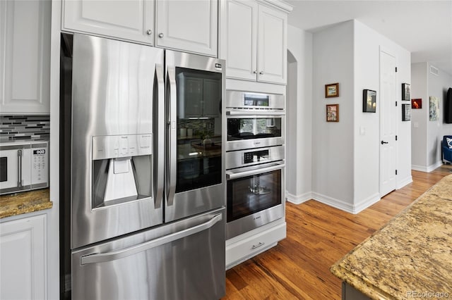 kitchen with wood finished floors, arched walkways, baseboards, and appliances with stainless steel finishes