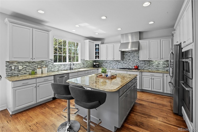kitchen featuring a breakfast bar area, white cabinetry, wall chimney range hood, tasteful backsplash, and appliances with stainless steel finishes