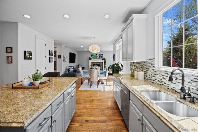 kitchen featuring recessed lighting, gray cabinetry, light wood finished floors, a sink, and a fireplace