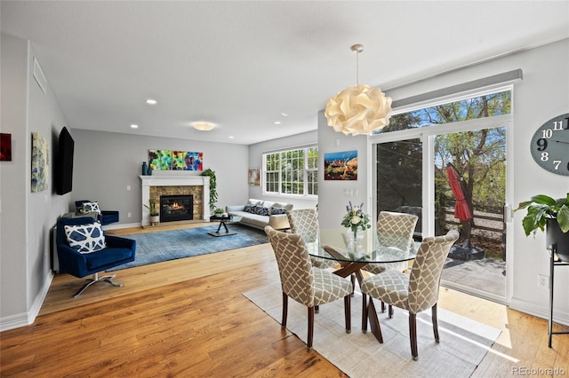dining room with baseboards, a stone fireplace, light wood-style floors, and visible vents