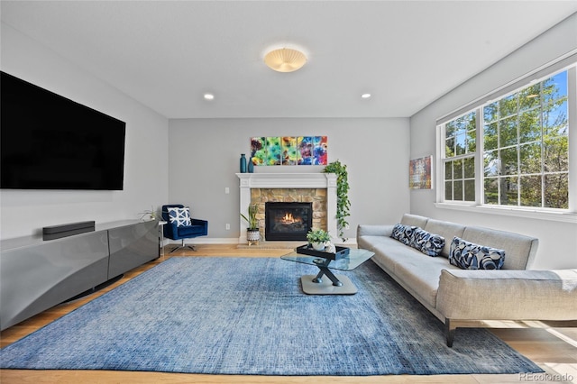 living room with wood finished floors, baseboards, a stone fireplace, and recessed lighting