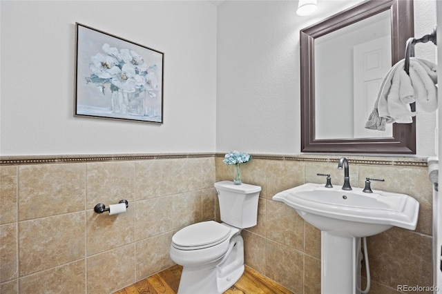 half bathroom with toilet, tile walls, wainscoting, and wood finished floors