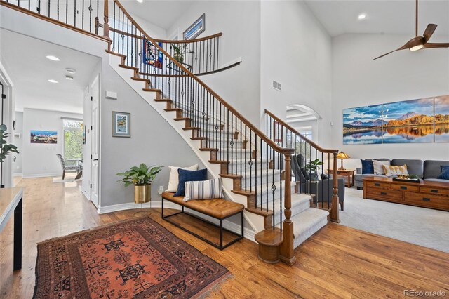 stairway featuring ceiling fan, visible vents, wood finished floors, and a high ceiling