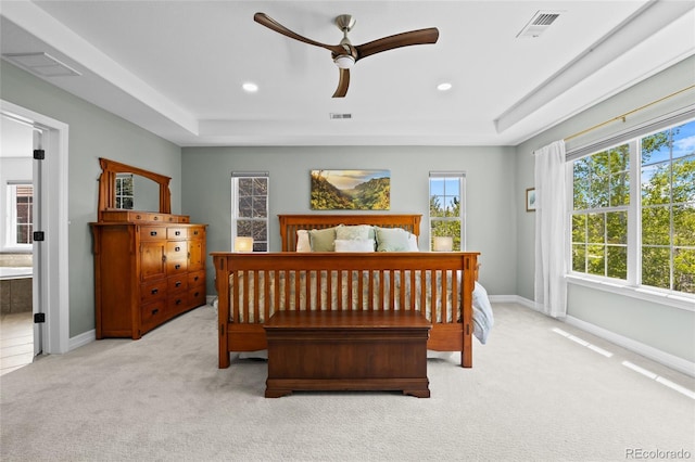 bedroom with a tray ceiling, light carpet, and visible vents