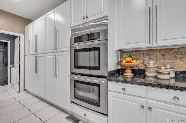 9856 Glenstone Trl, Highlands Ranch, CO 80130 - kitchen featuring stainless steel double oven, light tile patterned floors, white cabinetry, decorative backsplash, and dark stone countertops