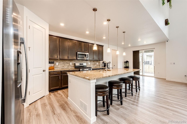 985 S Elk Way, Aurora, CO 80018 - kitchen with stainless steel appliances, light wood finished floors, dark brown cabinets, decorative backsplash, and a kitchen bar