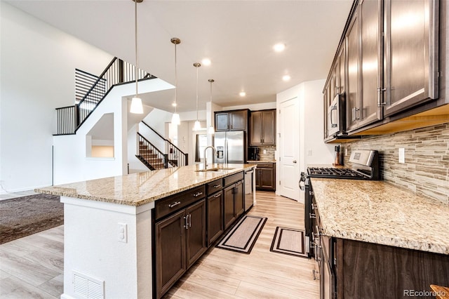 985 S Elk Way, Aurora, CO 80018 - kitchen featuring appliances with stainless steel finishes, dark brown cabinets, light wood-style flooring, tasteful backsplash, and light stone counters