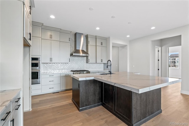 kitchen with a large island, sink, light stone counters, and wall chimney exhaust hood