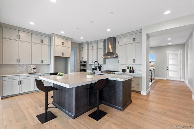 kitchen featuring stainless steel appliances, a kitchen island with sink, a breakfast bar area, and wall chimney range hood