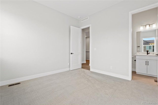 unfurnished bedroom featuring light carpet, sink, and ensuite bathroom