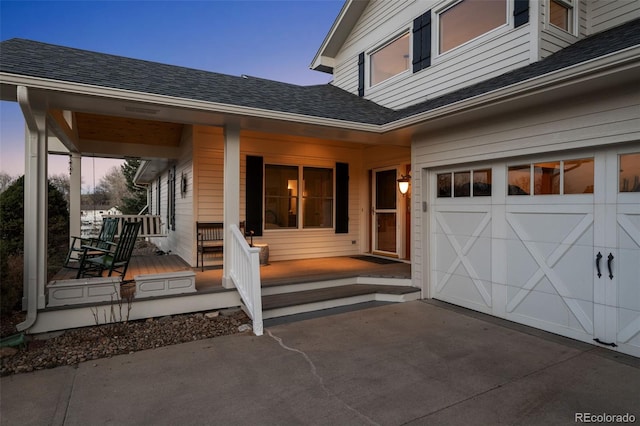 exterior entry at dusk featuring a garage and a porch