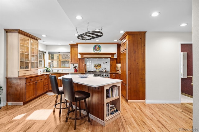 kitchen with a kitchen island, a kitchen breakfast bar, decorative backsplash, stove, and light wood-type flooring