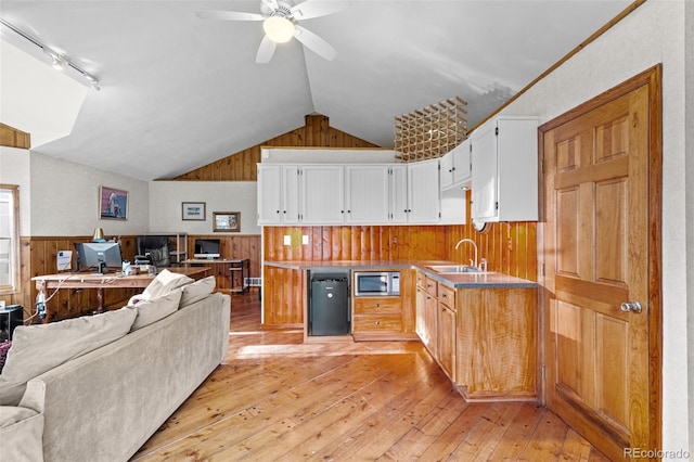 kitchen with vaulted ceiling, stainless steel microwave, sink, white cabinets, and light wood-type flooring