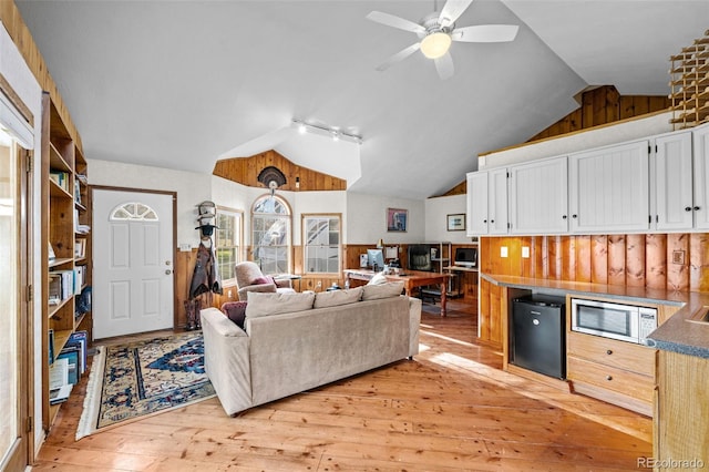 living room featuring lofted ceiling, light hardwood / wood-style flooring, ceiling fan, wooden walls, and track lighting