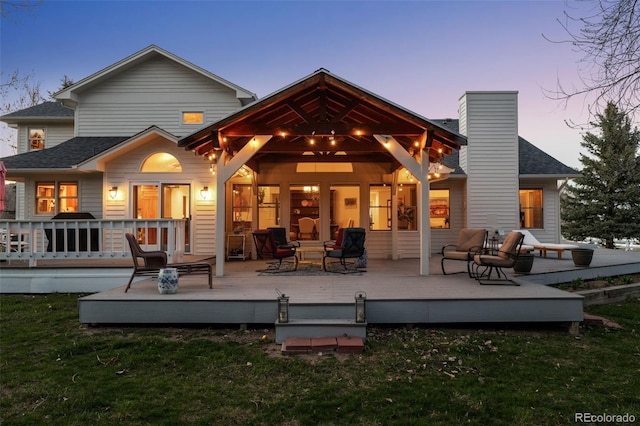 back house at dusk with a yard, a deck, and an outdoor living space with a fire pit