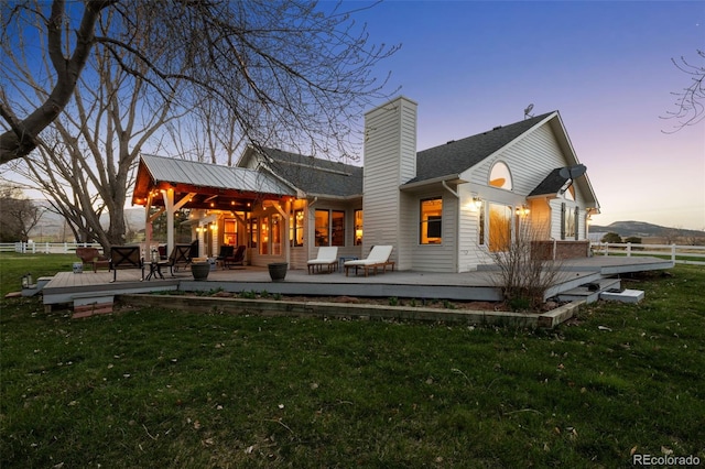 back house at dusk featuring a wooden deck and a yard