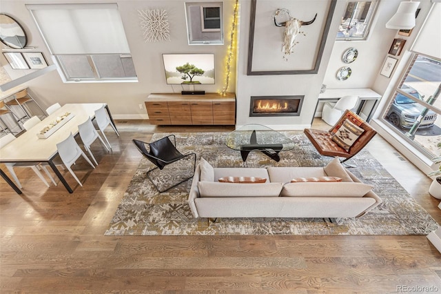living area with baseboards, a glass covered fireplace, and wood finished floors