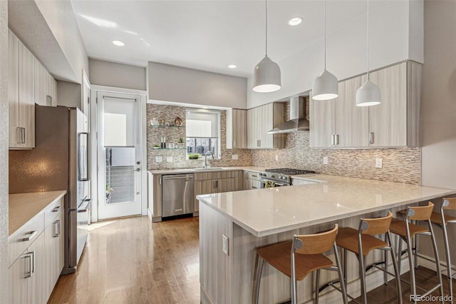 kitchen featuring decorative backsplash, appliances with stainless steel finishes, wood finished floors, a peninsula, and wall chimney exhaust hood