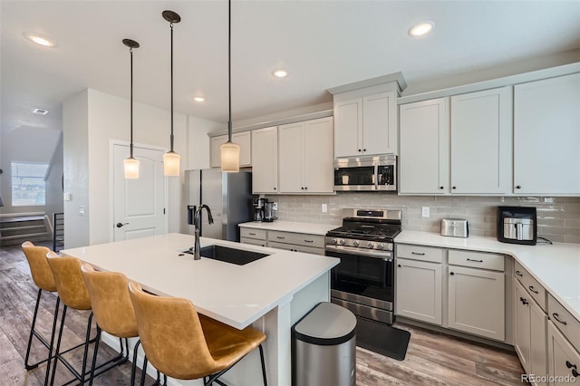 kitchen with an island with sink, appliances with stainless steel finishes, backsplash, pendant lighting, and sink