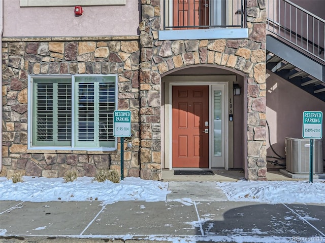 snow covered property entrance with stone siding and central AC unit