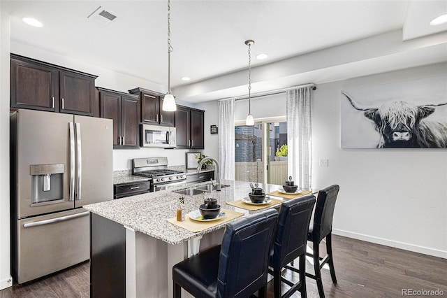 kitchen with appliances with stainless steel finishes, a kitchen breakfast bar, sink, decorative light fixtures, and an island with sink