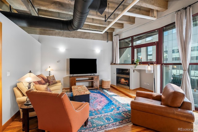 living area with a warm lit fireplace, baseboards, and wood finished floors