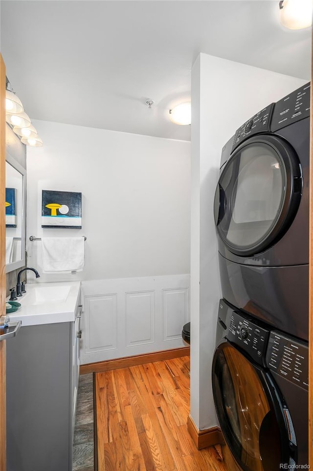 clothes washing area with stacked washer / drying machine, laundry area, a sink, and light wood finished floors