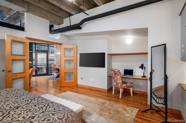 bedroom featuring built in desk, a high ceiling, and light wood-style floors