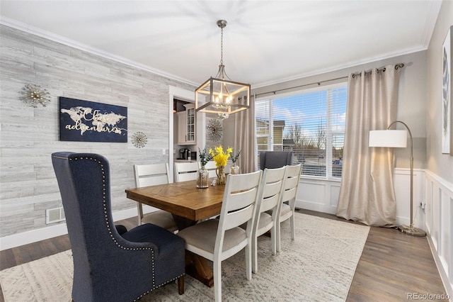 dining space featuring an accent wall, a chandelier, crown molding, and wood finished floors