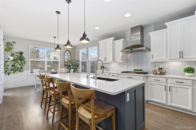 kitchen featuring wall chimney exhaust hood, dark wood-style flooring, white cabinets, and a sink