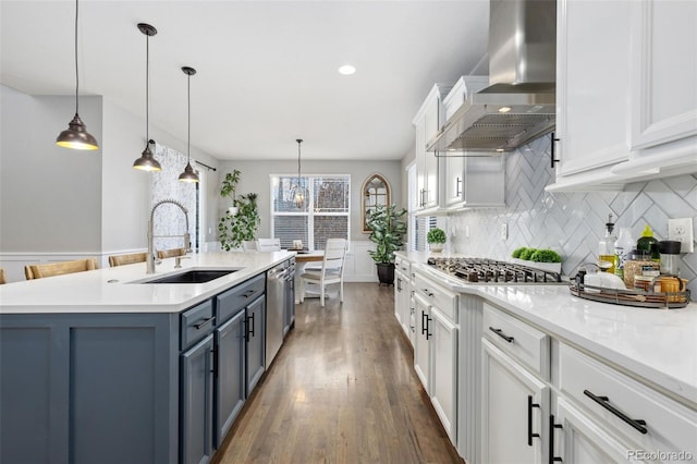 kitchen featuring a sink, light countertops, wall chimney range hood, white cabinetry, and backsplash