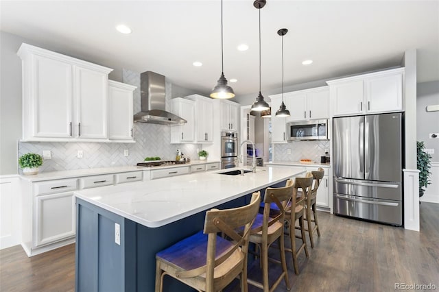 kitchen featuring white cabinets, wall chimney exhaust hood, dark wood-type flooring, stainless steel appliances, and a sink