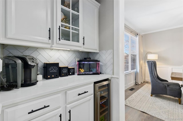 bar featuring beverage cooler, wood finished floors, wainscoting, backsplash, and crown molding