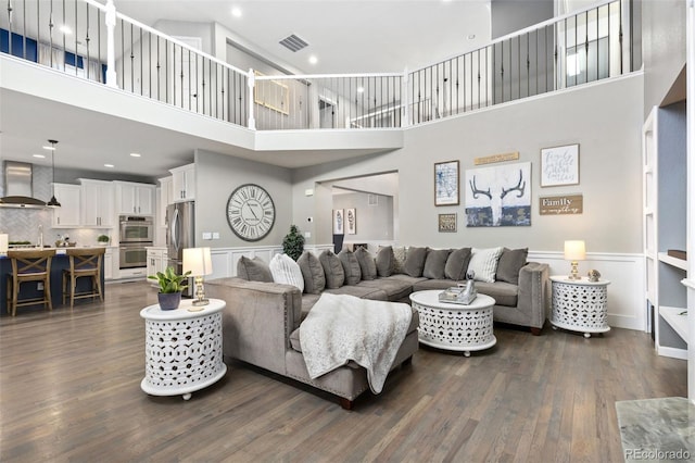 living room featuring dark wood-style floors, a high ceiling, a wainscoted wall, and visible vents