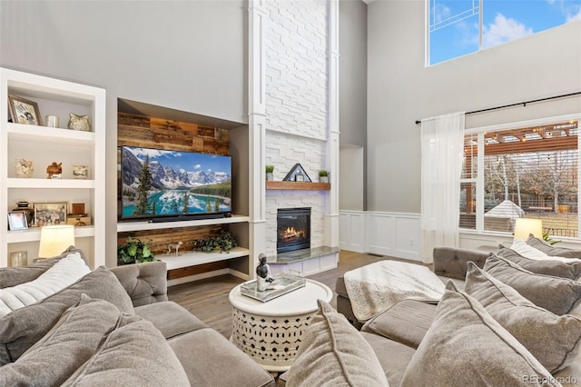 living room featuring built in features, a wainscoted wall, a fireplace, a towering ceiling, and wood finished floors