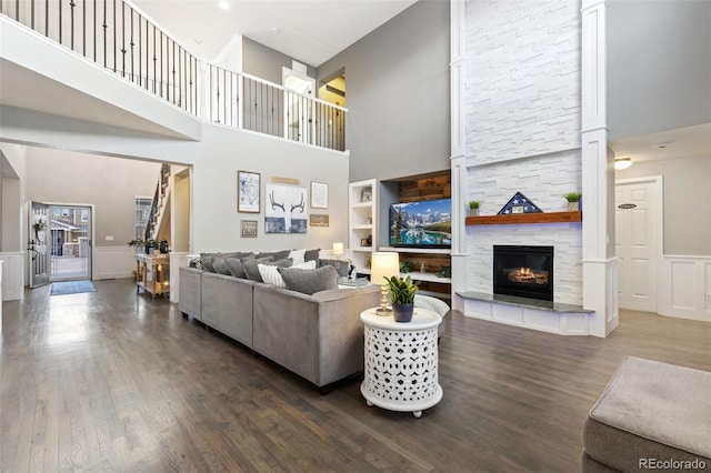 living room featuring a stone fireplace, a decorative wall, wood finished floors, built in features, and wainscoting