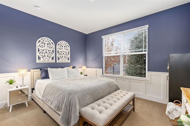 bedroom featuring a decorative wall, wainscoting, and light colored carpet