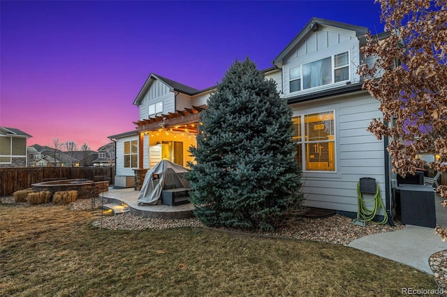 back of property at dusk with fence, board and batten siding, and a patio