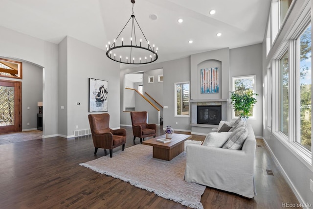 living room featuring a notable chandelier, dark wood-type flooring, a towering ceiling, and plenty of natural light