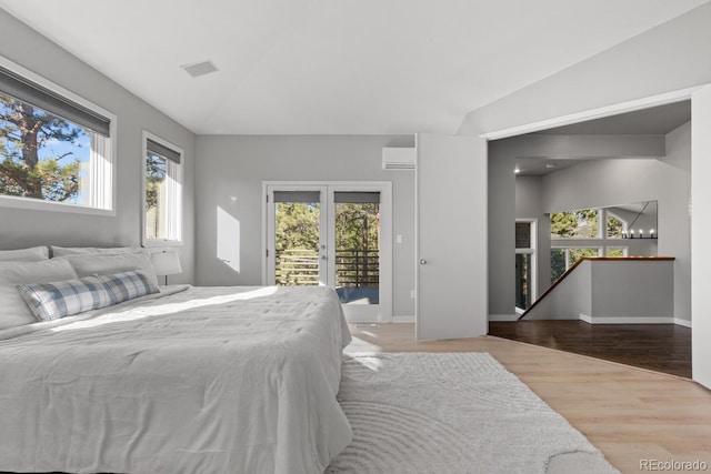 bedroom with access to outside, hardwood / wood-style flooring, a wall unit AC, and multiple windows