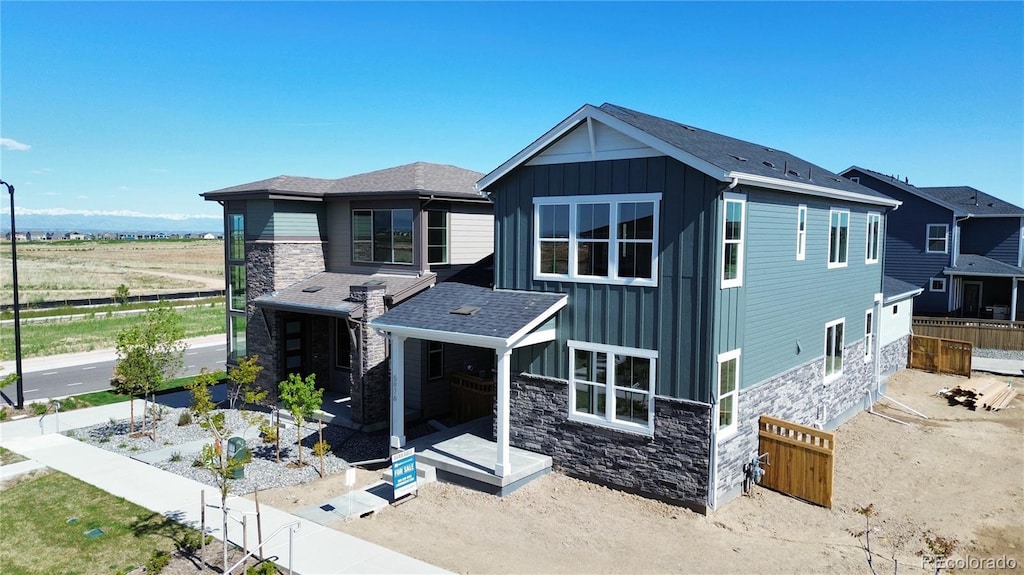 view of front of house with fence, board and batten siding, stone siding, and roof with shingles